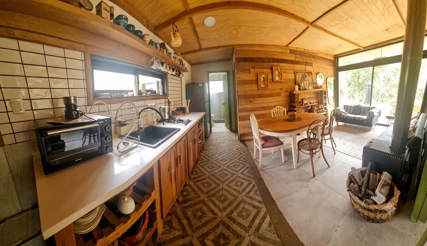 Estar y comedor de la casa, con estufa a leña y mesas junto a las puertas al deck